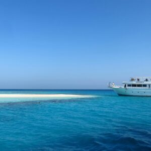 A scenic view of a luxury yacht by a pristine, sandy island in Egypt's vibrant blue waters.